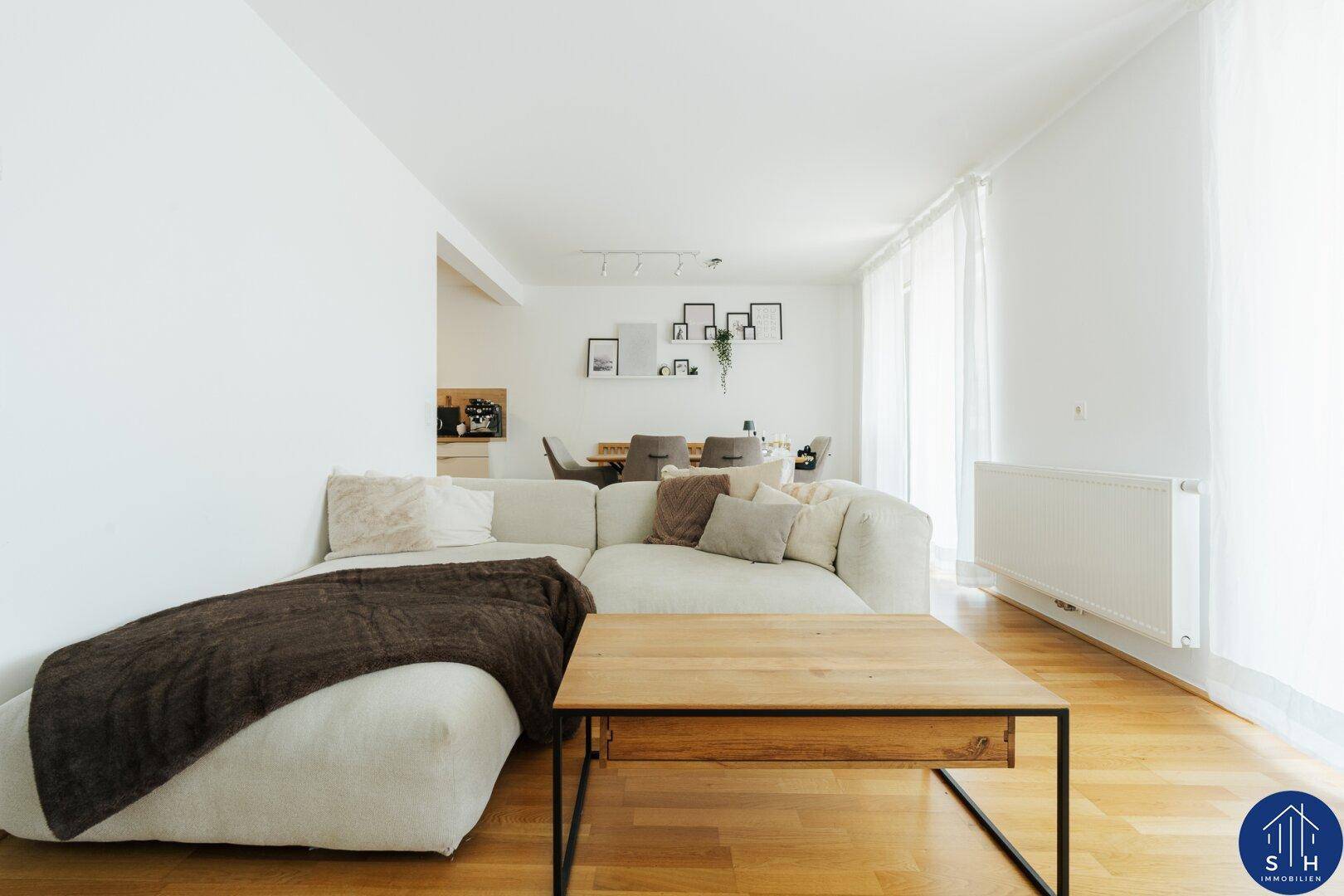 Heller Wohnbereich mit großem Sofa, Holztisch und Blick auf den Essbereich und die offene Küche.