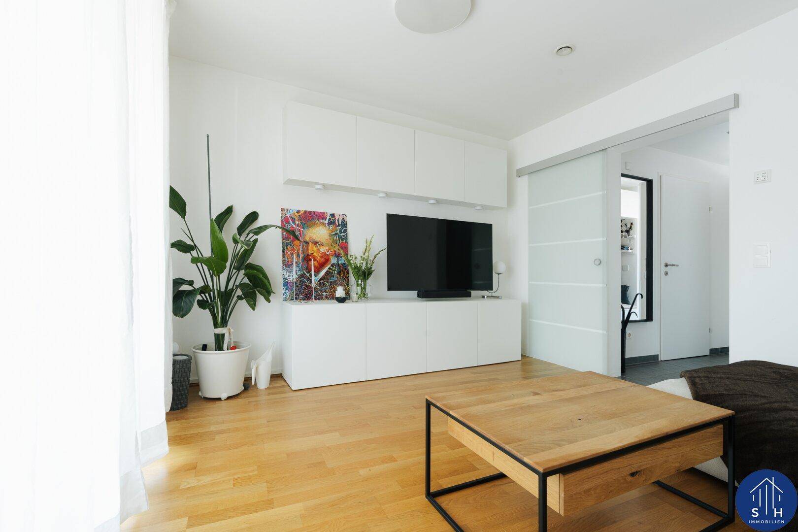 Modernes Wohnzimmer mit TV-Möbeln, Zimmerpflanze und Holztisch, durch Glasschiebetür verbunden.