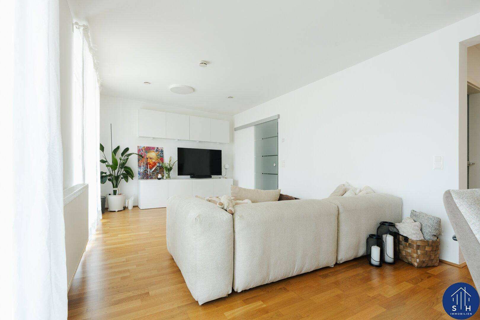 Geräumiges Wohnzimmer mit beigem Sofa, Holzboden und moderner TV-Wand in hellem Ambiente.