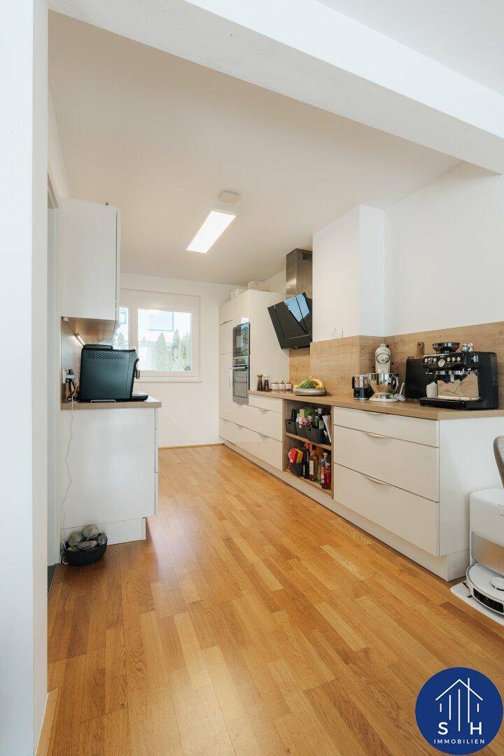 Moderne Küche mit hellen Holz-Arbeitsplatten, weißen Schränken und Fenster mit viel Tageslicht.