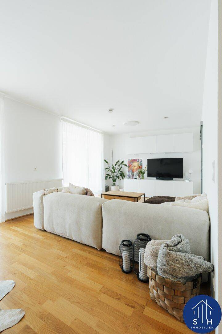 Helles Wohnzimmer mit großem beigem Sofa, Holzboden und moderner TV-Wand.