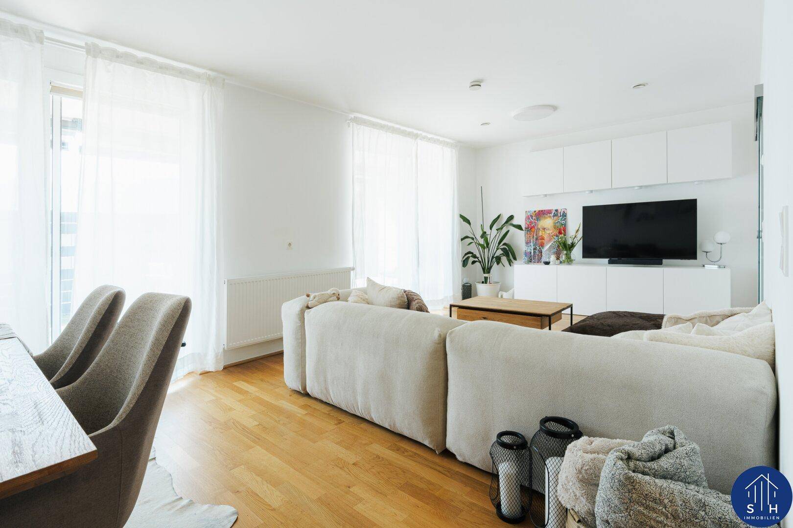 Offener Wohn-Essbereich mit großem Sofa, Holzboden und moderner TV-Wand in hellem Ambiente.