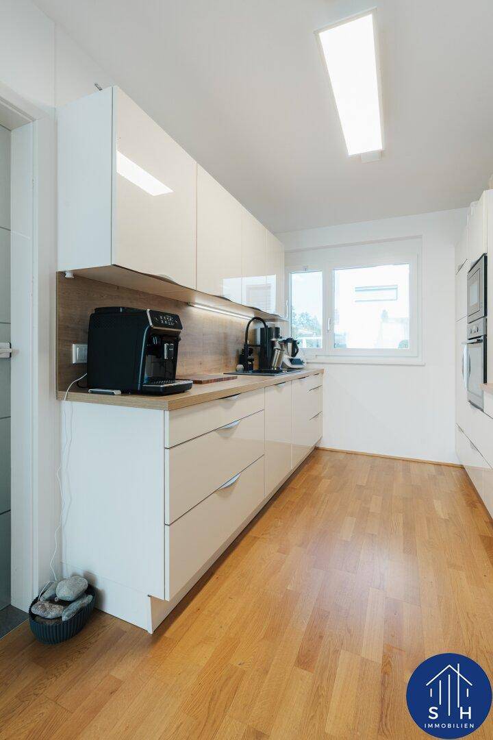 Moderne Küche mit weißen Hochglanzschränken, Holzakzenten und integrierten Geräten.