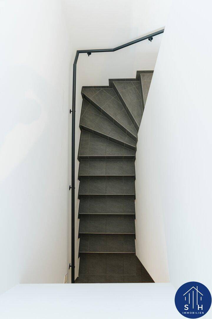 Blick von oben auf die moderne Treppe mit grauen Fliesen und schwarzem Handlauf.