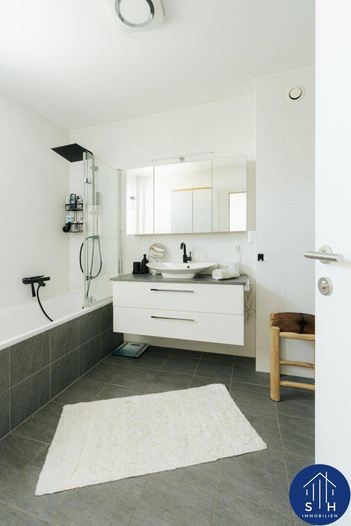 Modernes Badezimmer mit Badewanne, Dusche und Einzelwaschbecken auf grauen Fliesen.