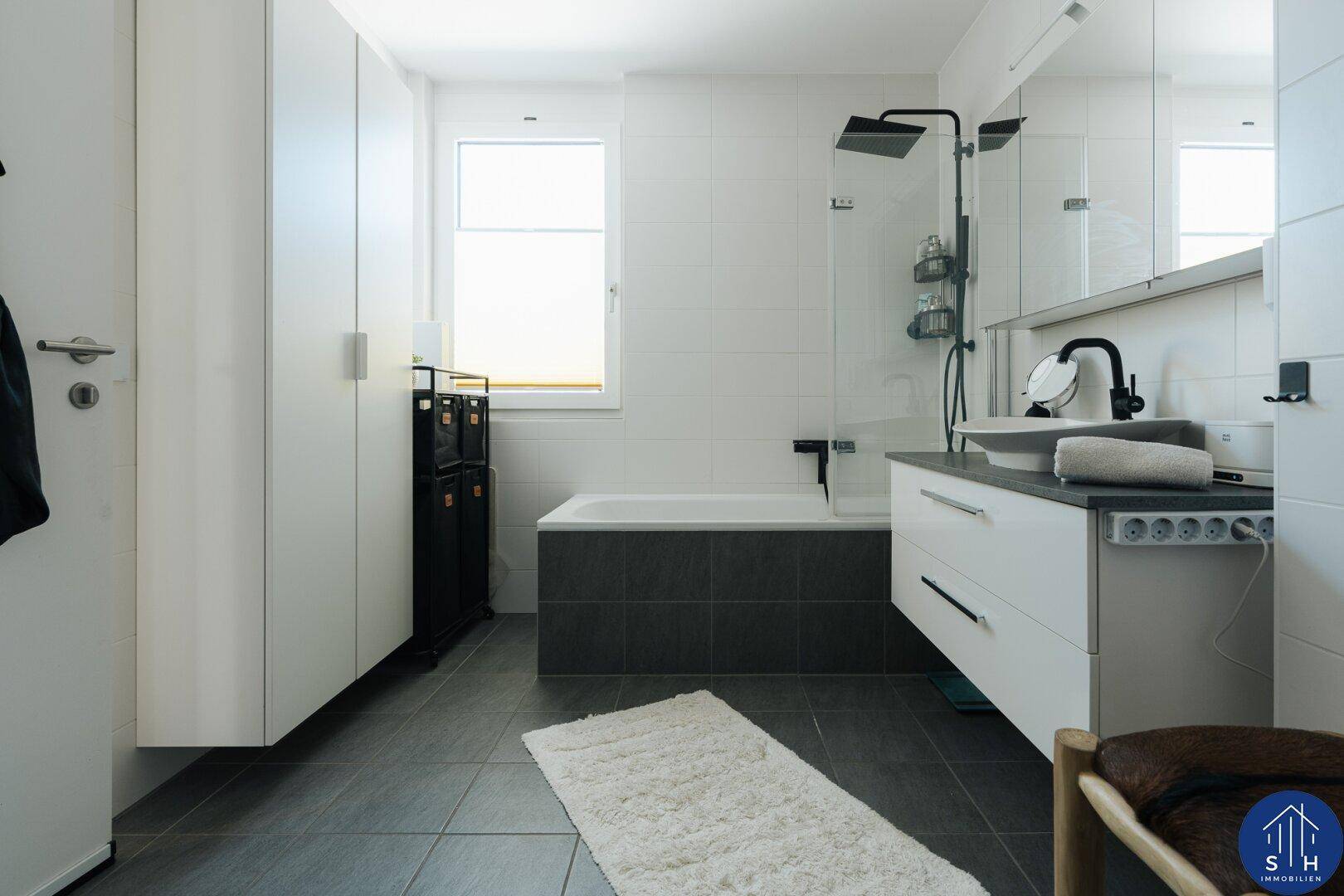 Helles Badezimmer mit Badewanne, Dusche, Einzelwaschbecken und praktischen Einbauschränken.