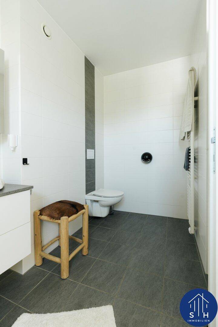 Badezimmer mit wandhängendem WC, beheiztem Handtuchhalter und modernen Fliesen.