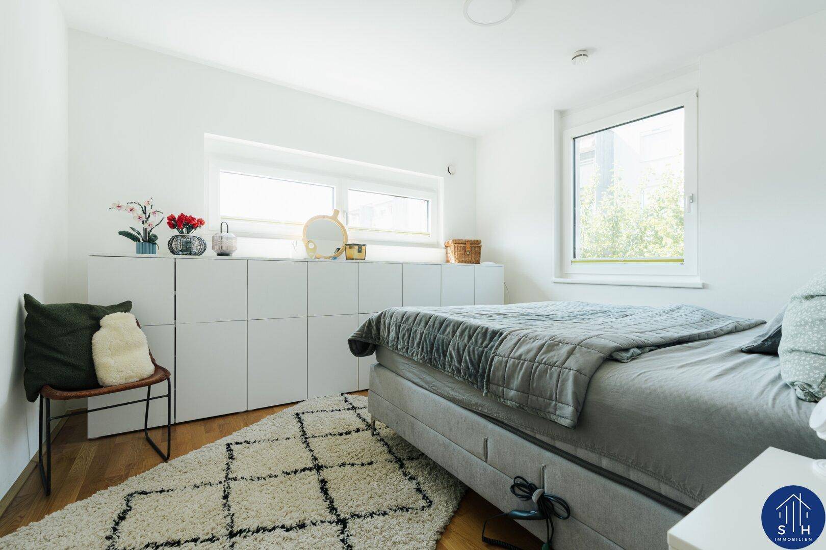 Gemütliches Schlafzimmer mit Doppelbett, weißen Schränken und zwei Fenstern für viel Licht.