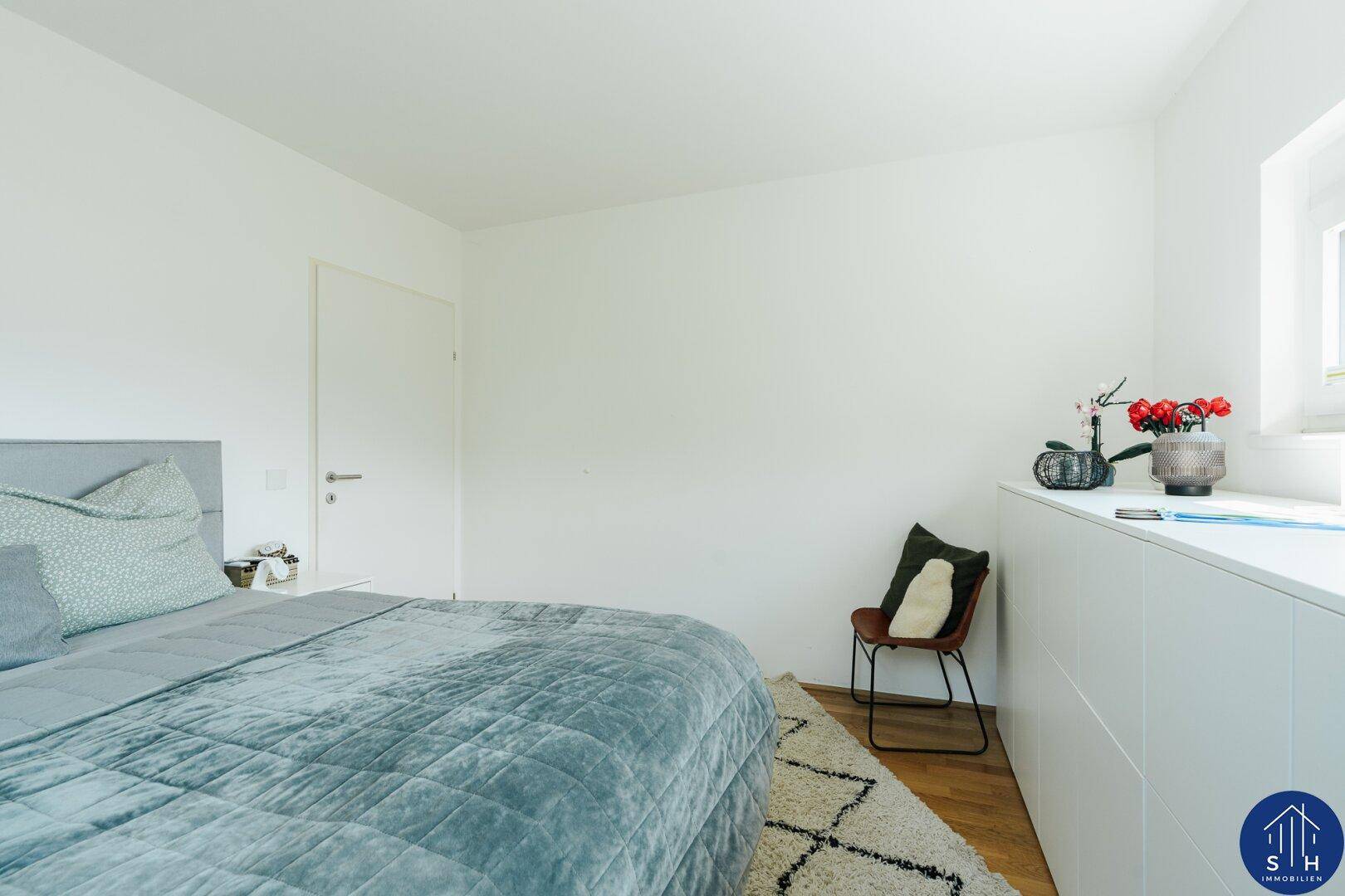 Schlafzimmer mit bequemen Bett, Stuhl und praktischen weißen Einbauschränken.