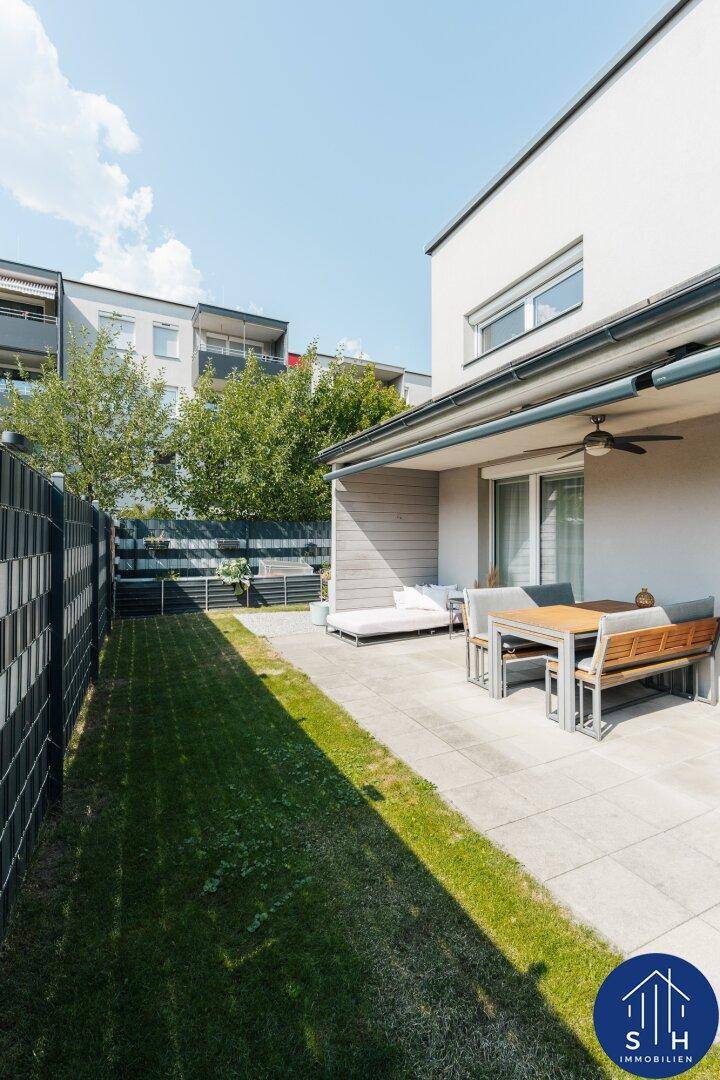 Sonniger Außenbereich mit gepflasterter Terrasse, Gartenmöbeln und kleinem Rasenstück.