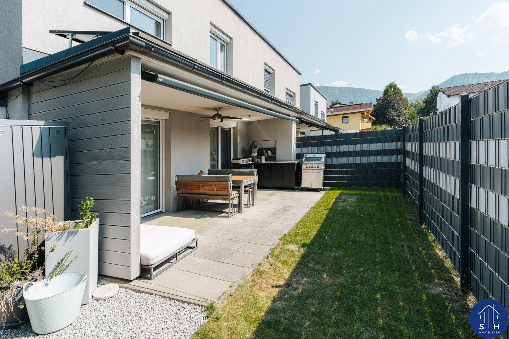 Sonniger Gartenbereich mit gepflasterter Terrasse, Essplatz im Freien und Grill.