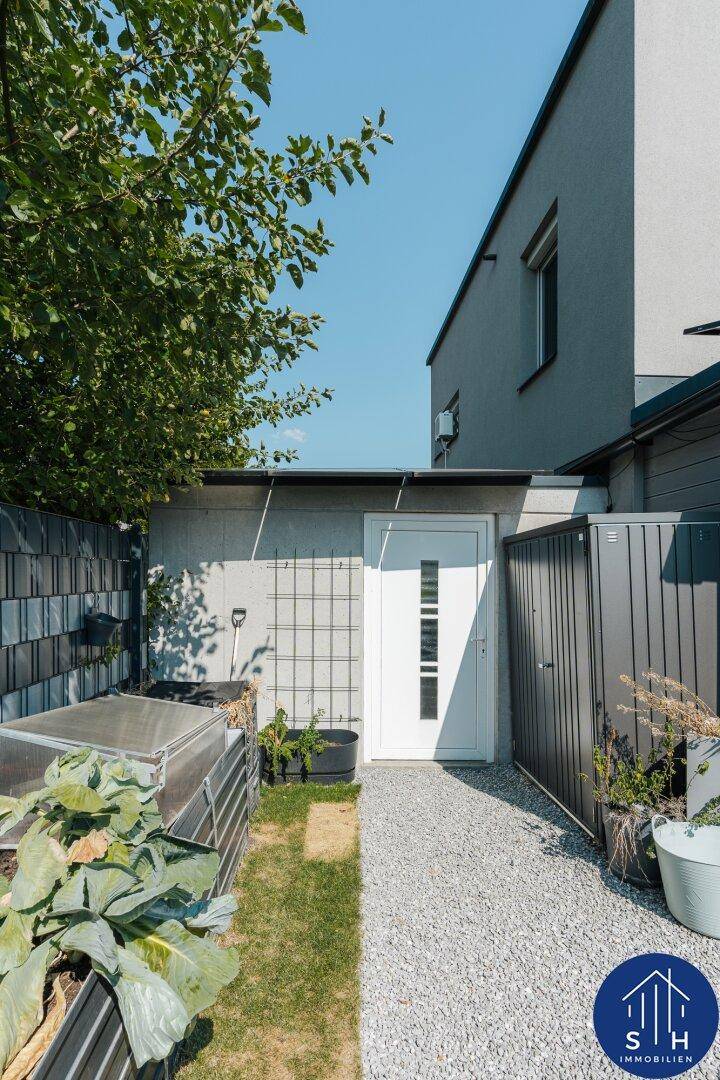 Seitlicher Gartenweg mit Hochbeet und Zugang zu einem Nebeneingang des Hauses.