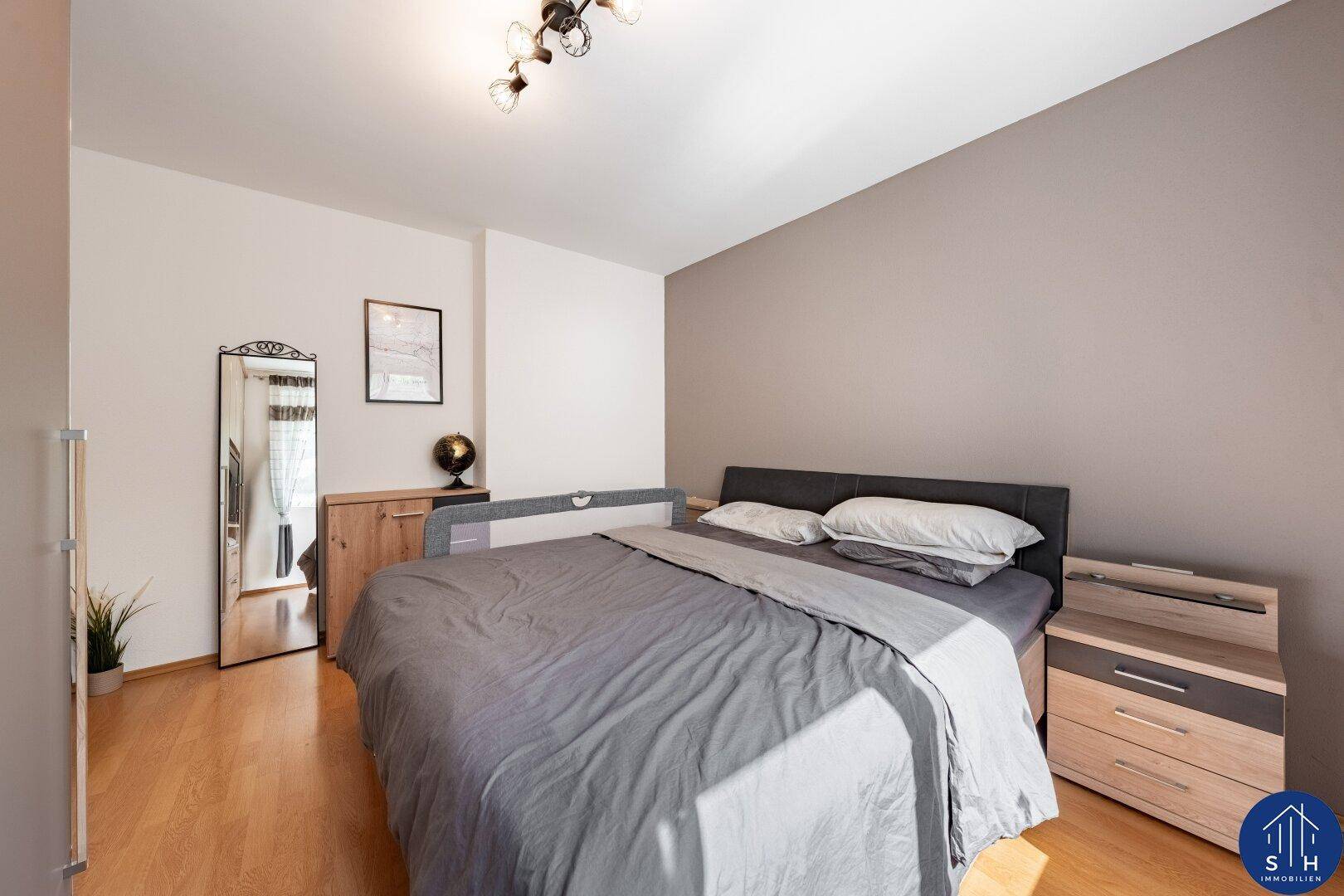 Gemütliches Schlafzimmer mit Holzboden, Doppelbett und einem großen Spiegel.