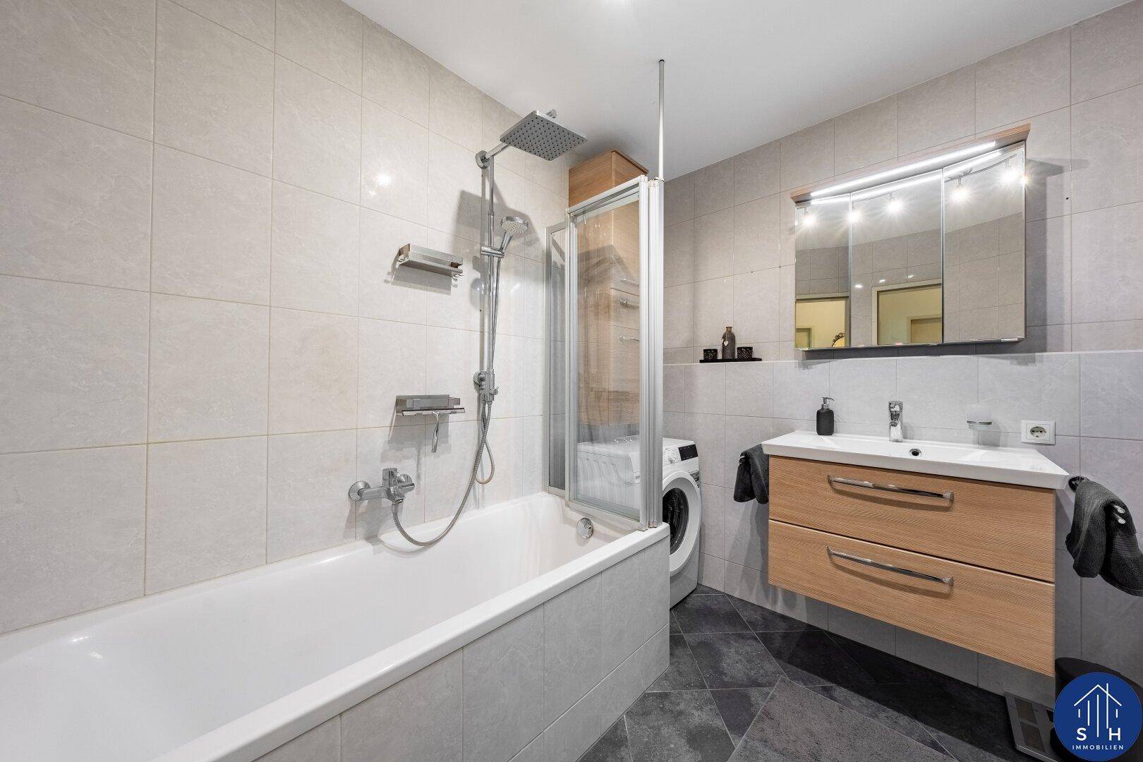 Modernes Badezimmer mit Badewanne, Duschfunktion, Waschbecken und Waschmaschine.