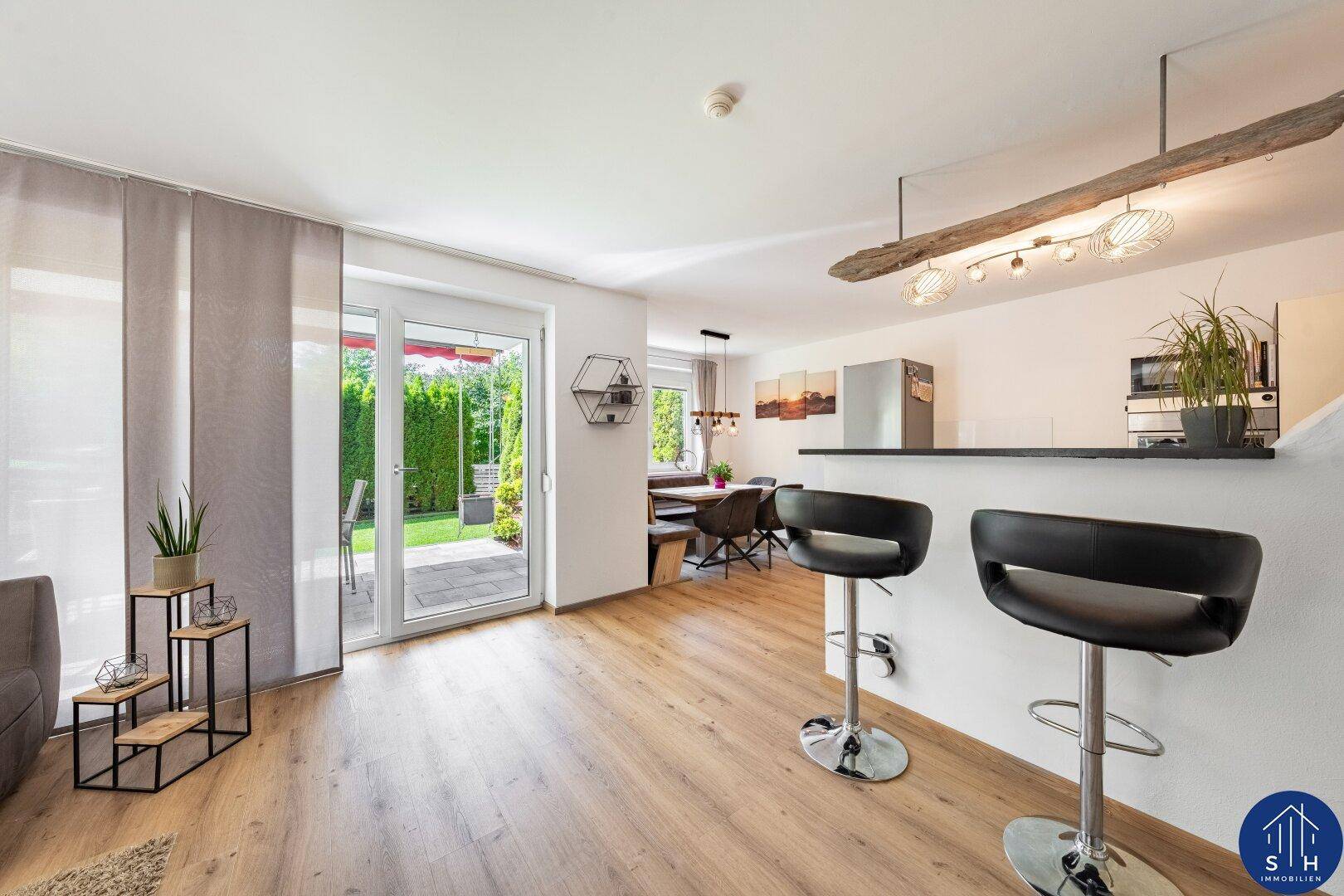 Offener Wohnbereich mit Frühstücksbar, Holzboden und Zugang zur Terrasse und zum Garten.