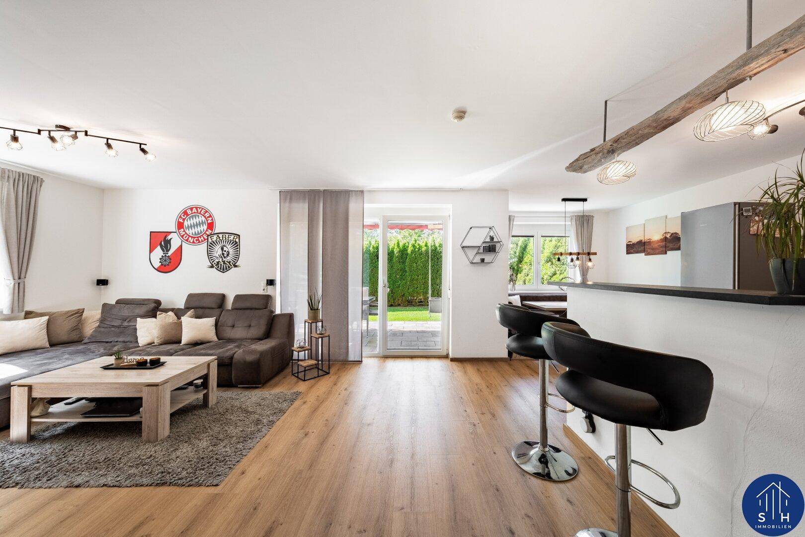 Geräumiger Wohnbereich mit großem Sofa, Holzboden und direktem Zugang zum grünen Garten.