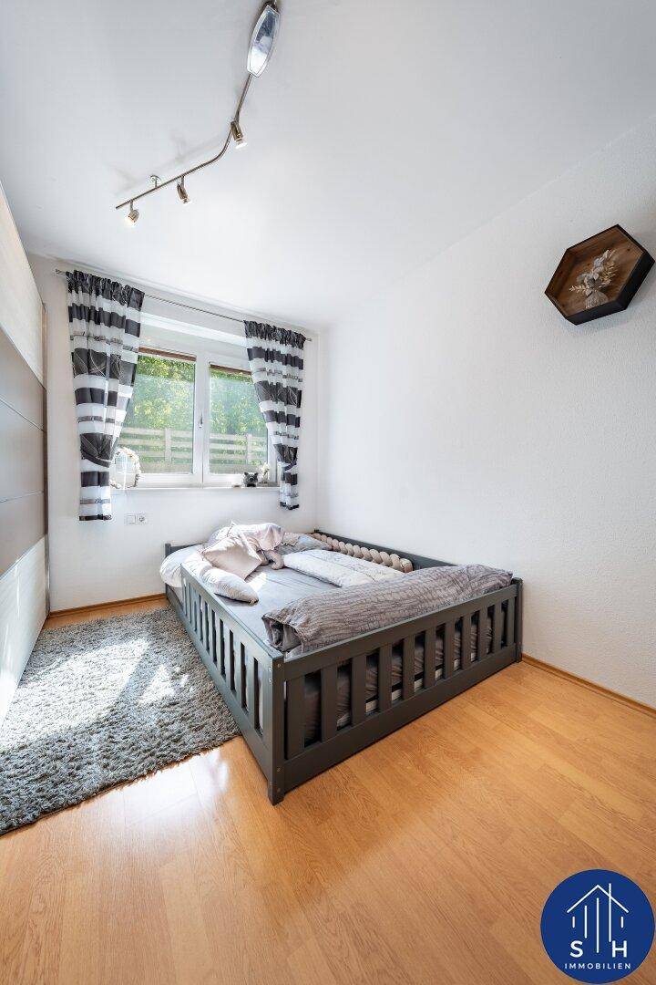 Helles Schlafzimmer mit Holzboden, Fenster und gestreiften Vorhängen.