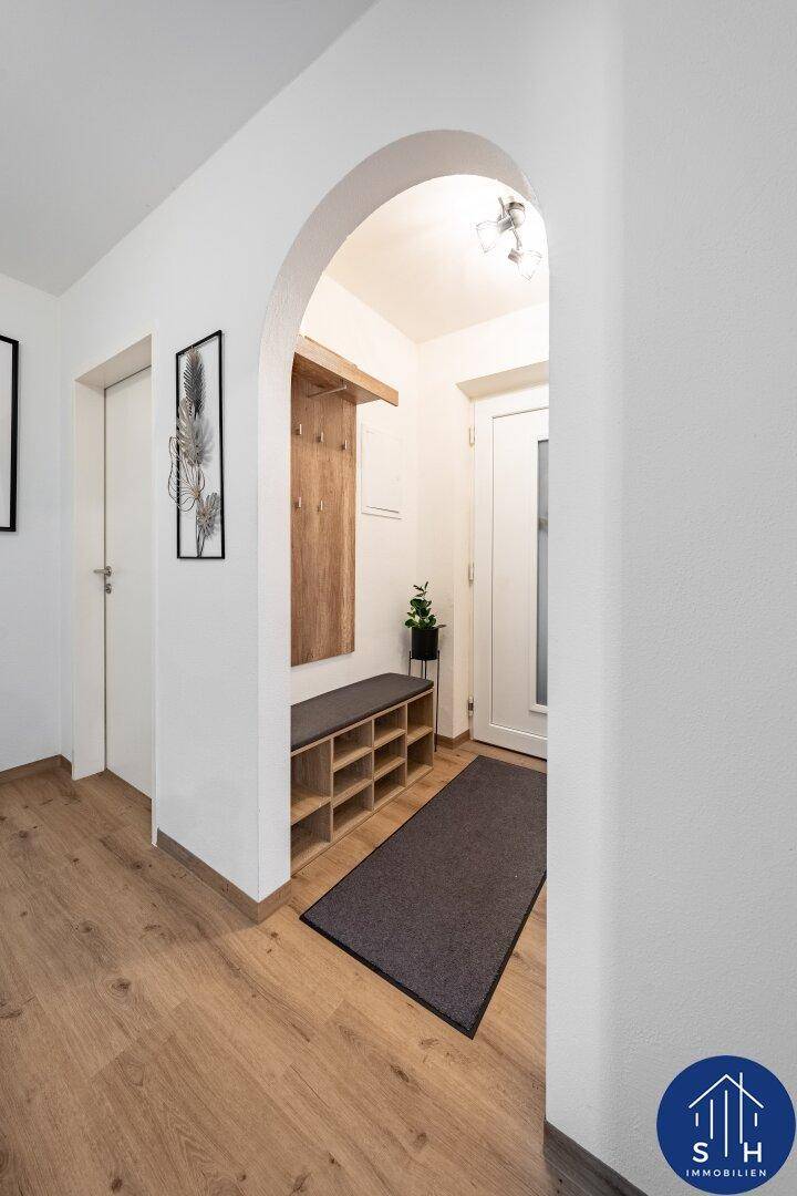 Heller Eingangsbereich mit Holzboden, Garderobe und einem dekorativen Bogen.