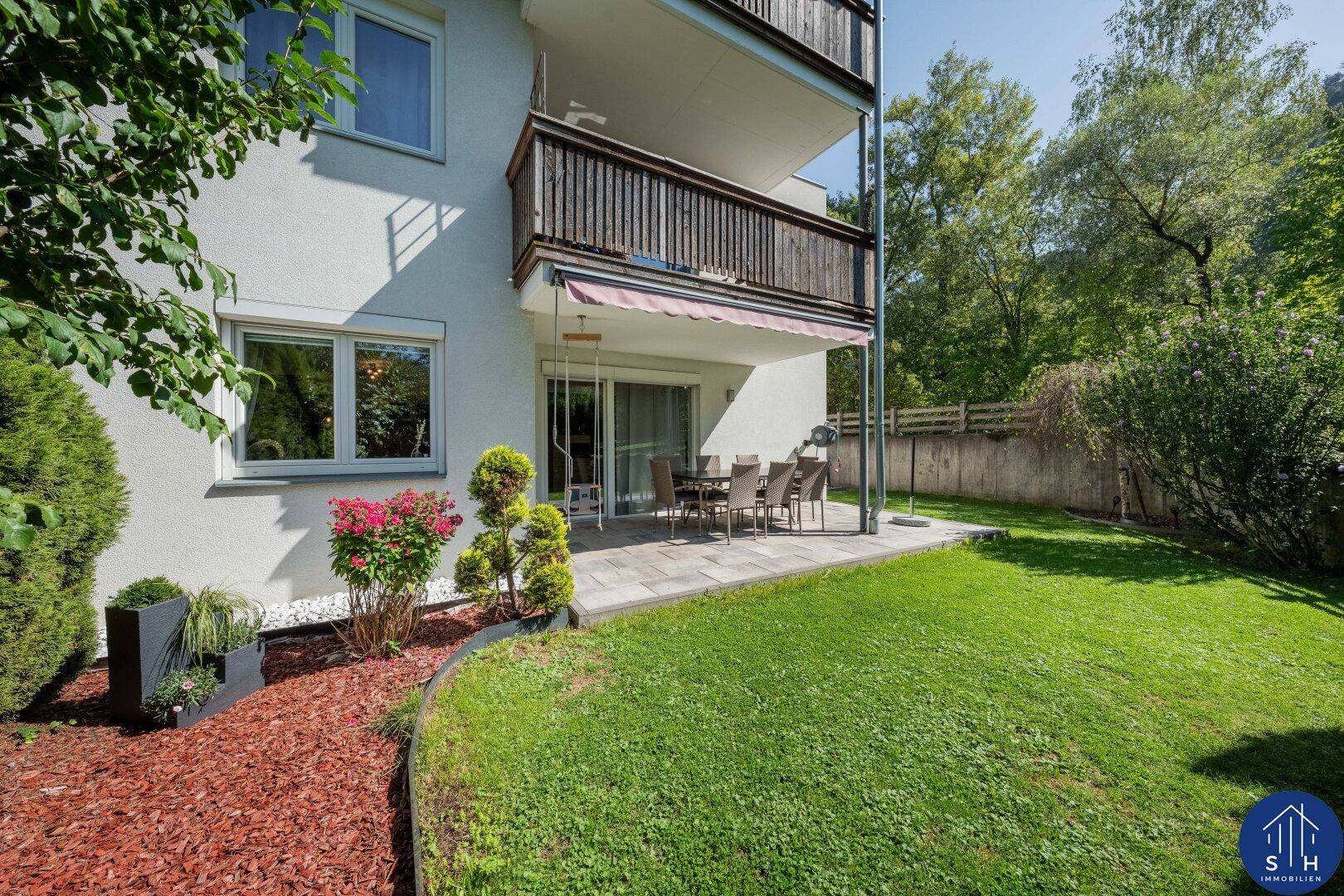 Außenansicht des Gebäudes mit Terrasse, Rasenfläche und Balkonen in einer grünen Umgebung.