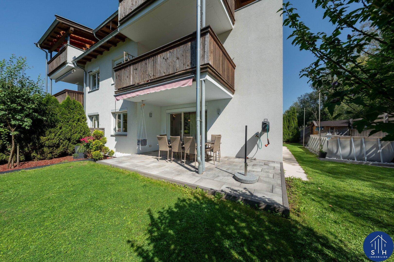 Außenansicht des Gebäudes mit Terrasse, Rasen und einem sichtbaren Pool im Hintergrund.