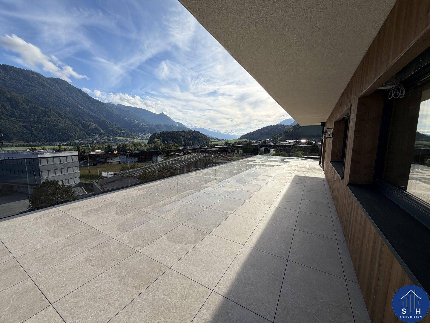Weitläufige Terrasse mit Fliesenboden und Glasbrüstung, bietet einen Panoramablick auf die Bergkette und das Tal.