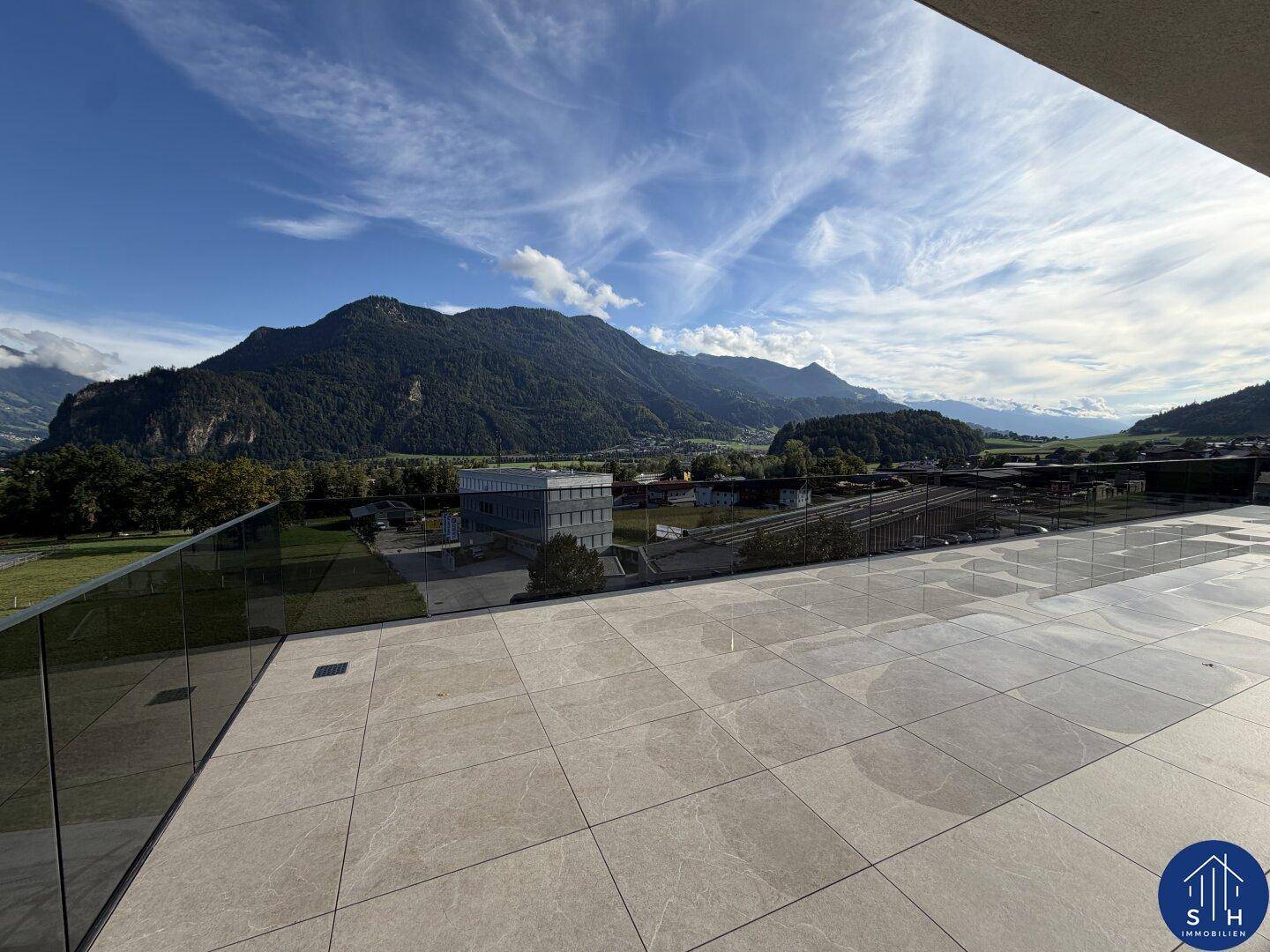 Weitläufige Terrasse mit Fliesenboden und Glasbrüstung, bietet einen Panoramablick auf die Bergkette und das Tal.