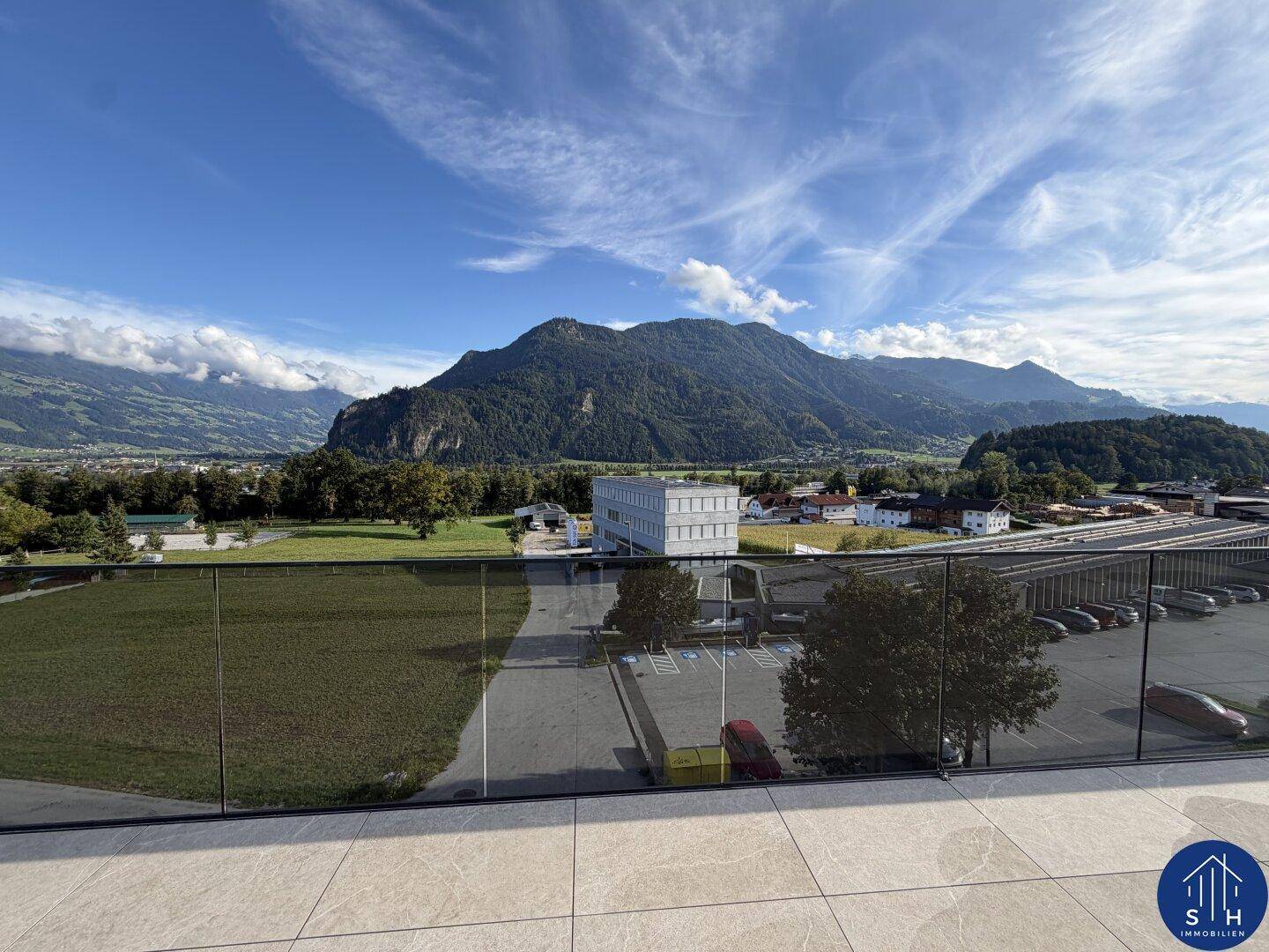Weitläufige Terrasse mit Fliesenboden und Glasbrüstung, bietet einen Panoramablick auf die Bergkette und das Tal.