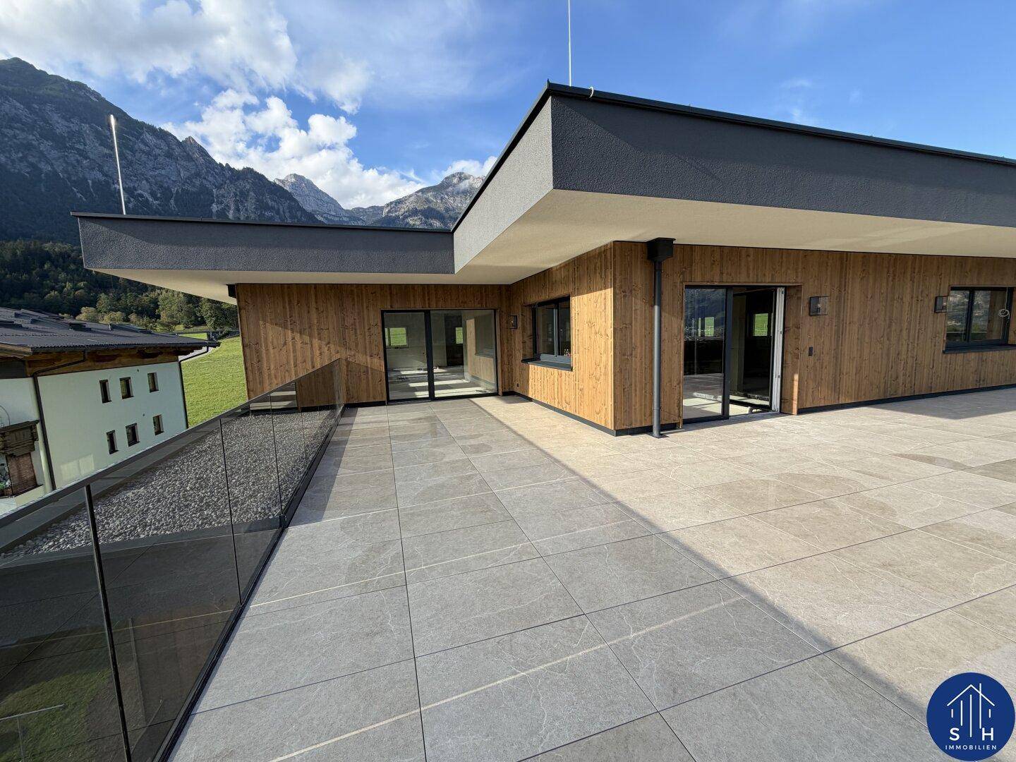 Großzügige Dachterrasse mit Fliesenboden und Holzfassade, bietet einen weiten Blick auf die umliegende Bergwelt.