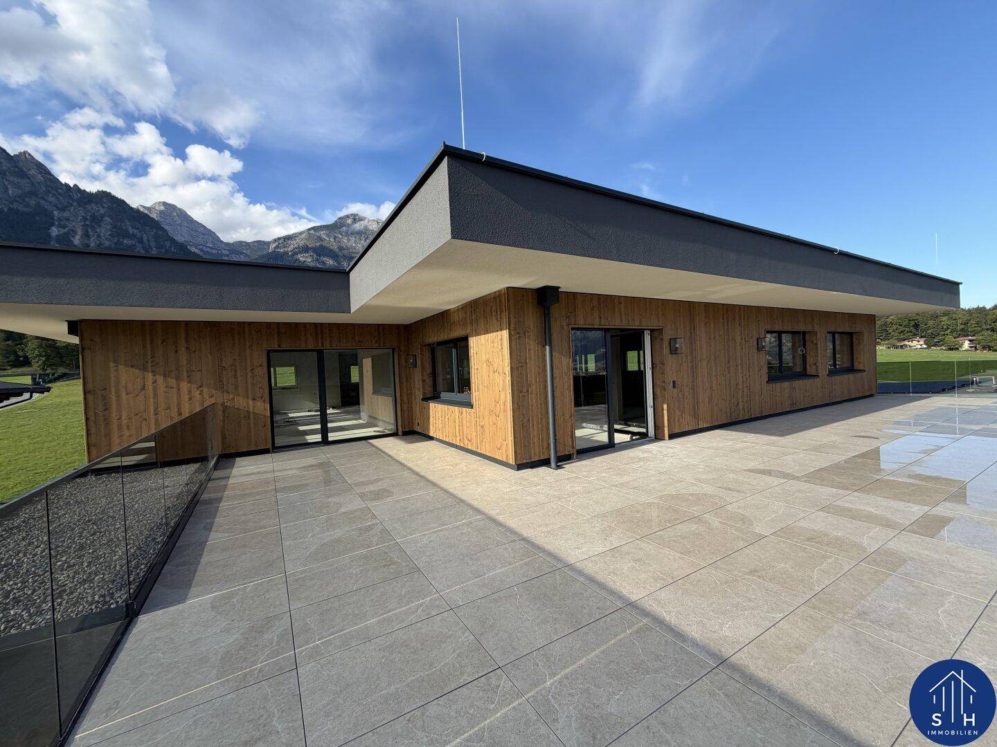 Großzügige Dachterrasse mit Fliesenboden und Holzfassade, bietet einen weiten Blick auf die umliegende Bergwelt.