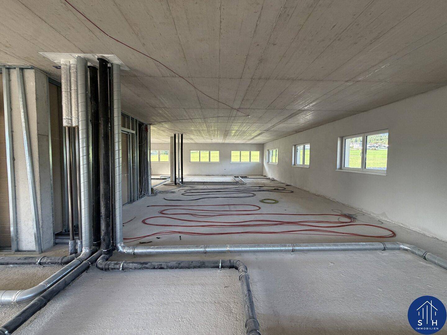 Großer, offener Raum im Rohbau mit sichtbaren Leitungen und Fußbodenheizung, bereit für den Ausbau.
