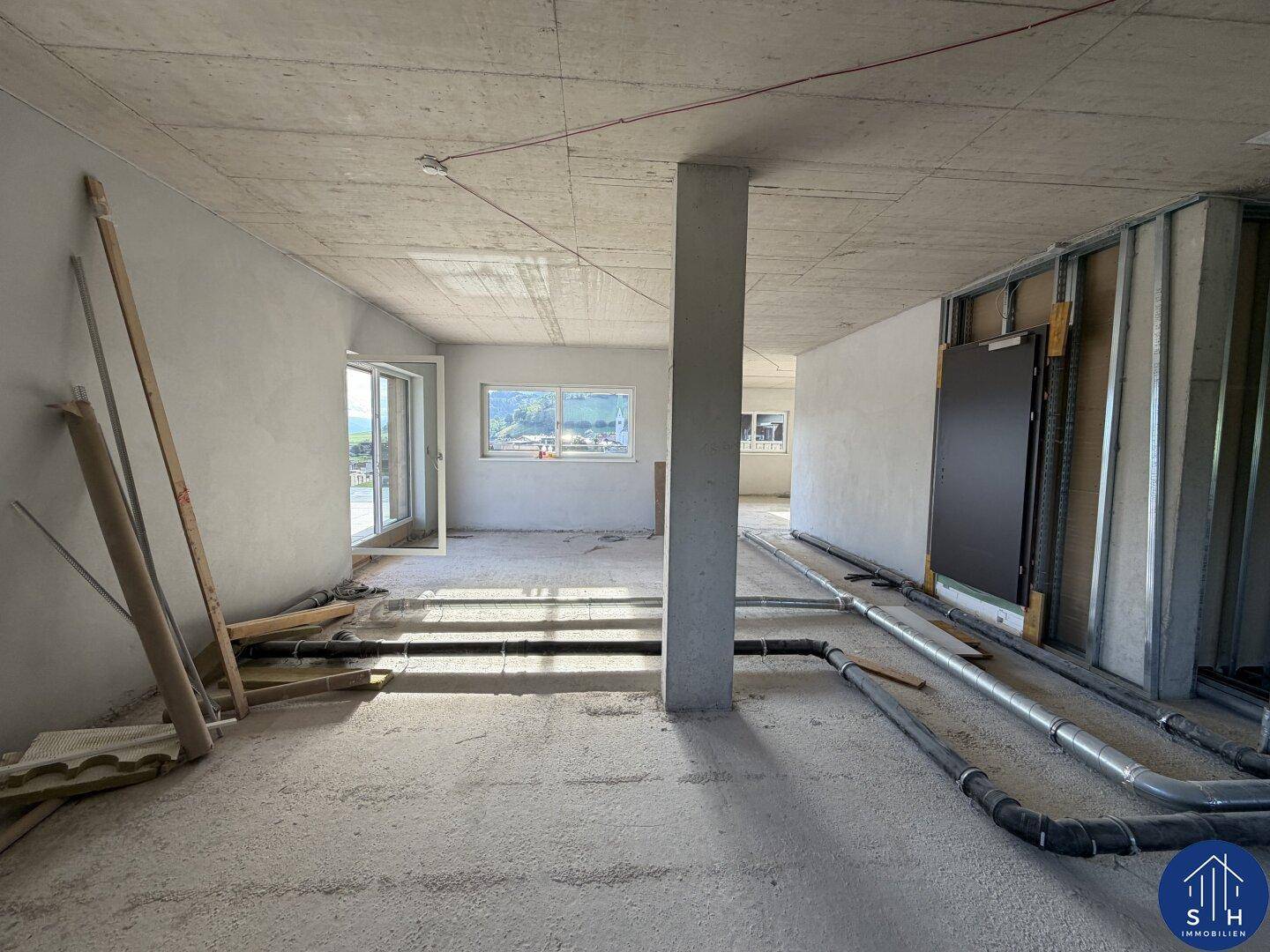 Großer, offener Raum im Rohbau mit sichtbaren Leitungen und Fußbodenheizung, bereit für den Ausbau.