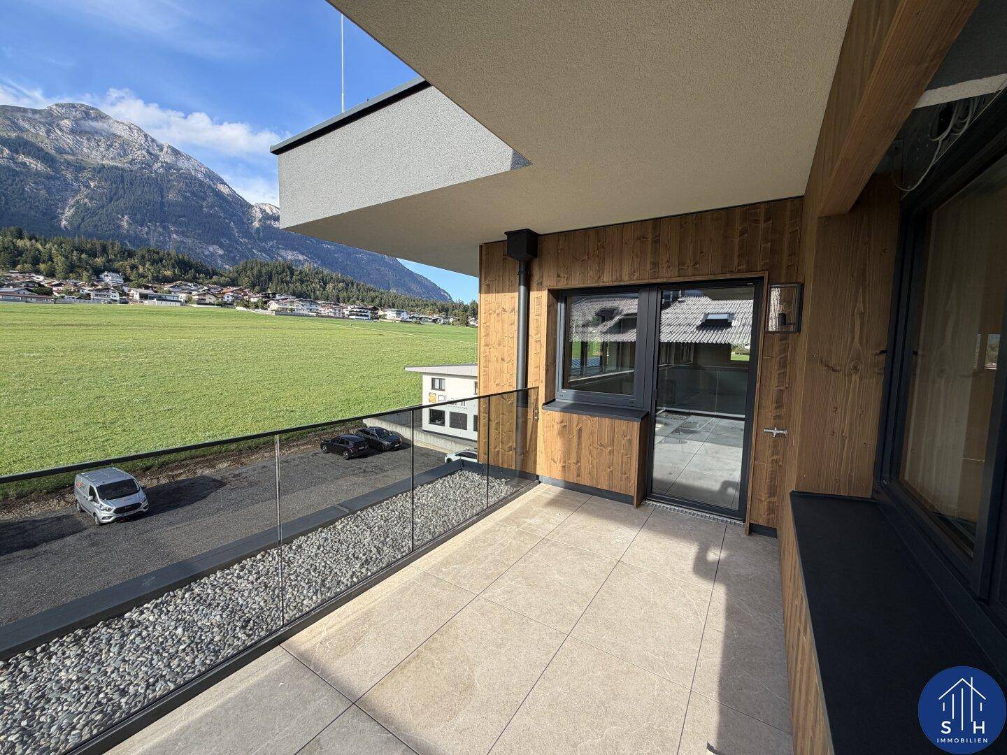 Kleinerer Balkon mit Glasgeländer und Kiesbett, bietet einen direkten Blick auf grüne Felder und Berge.
