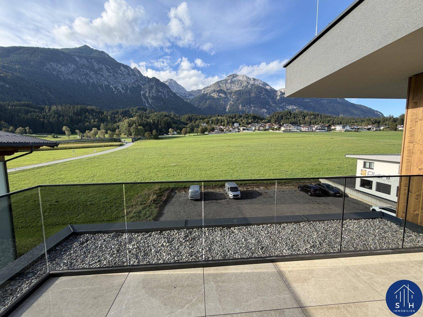 Kleinerer Balkon mit Glasgeländer und Kiesbett, bietet einen direkten Blick auf grüne Felder und Berge.