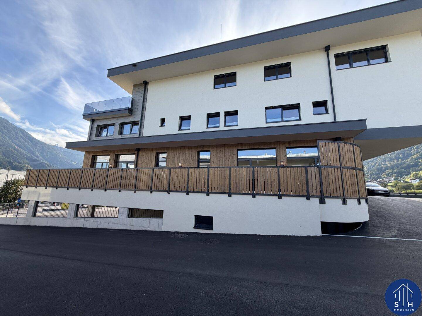Moderne Gebäudefassade mit Holzverkleidung und großen Fenstern, umgeben von einer bergigen Landschaft.