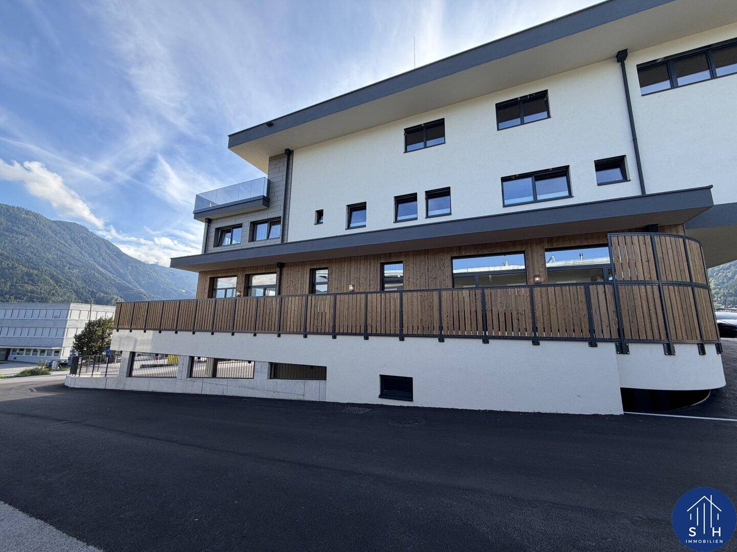 Moderne Gebäudefassade mit Holzverkleidung und großen Fenstern, umgeben von einer bergigen Landschaft.