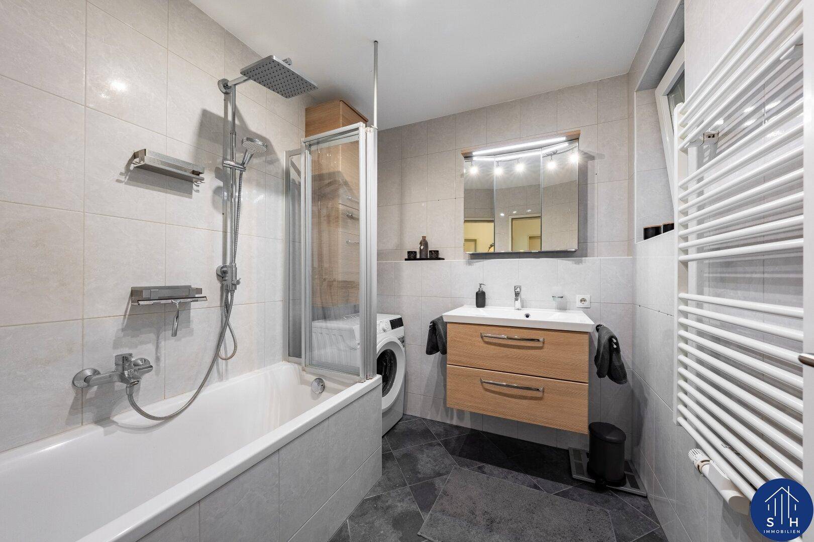 Modernes Badezimmer mit Badewanne, Regendusche, Waschbeckenunterschrank und beheiztem Handtuchhalter.