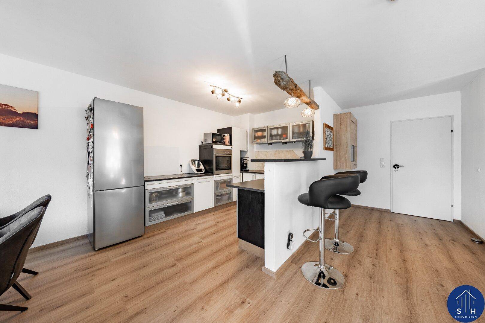 Offene Küche mit modernen Einbaugeräten, Kücheninsel mit Barhockern und hellem Laminatboden.