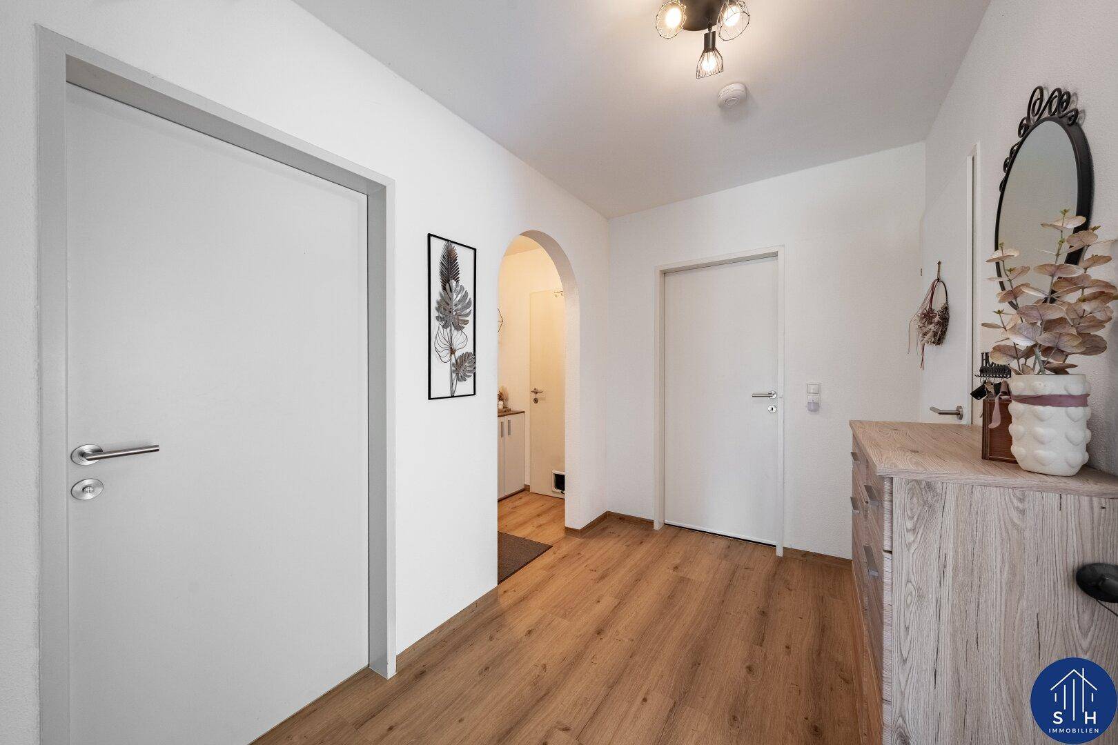 Heller Flur mit Laminatboden, einer Kommode und einem dekorativen Spiegel an der Wand.