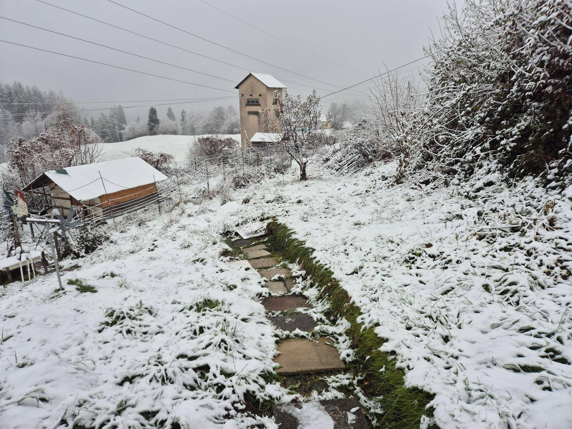 Verschneiter Steinpfad durch einen Hang mit Blick auf ein entferntes Gebäude in der Winterlandschaft.