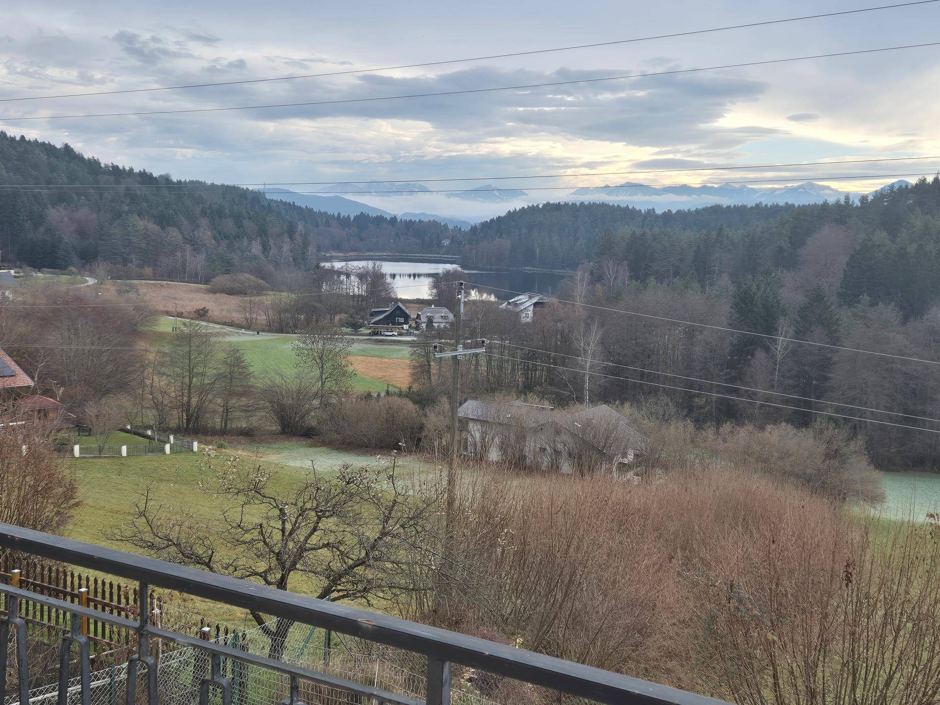 Panoramablick auf einen See, umgeben von Wäldern und Bergen unter einem bewölkten Himmel.