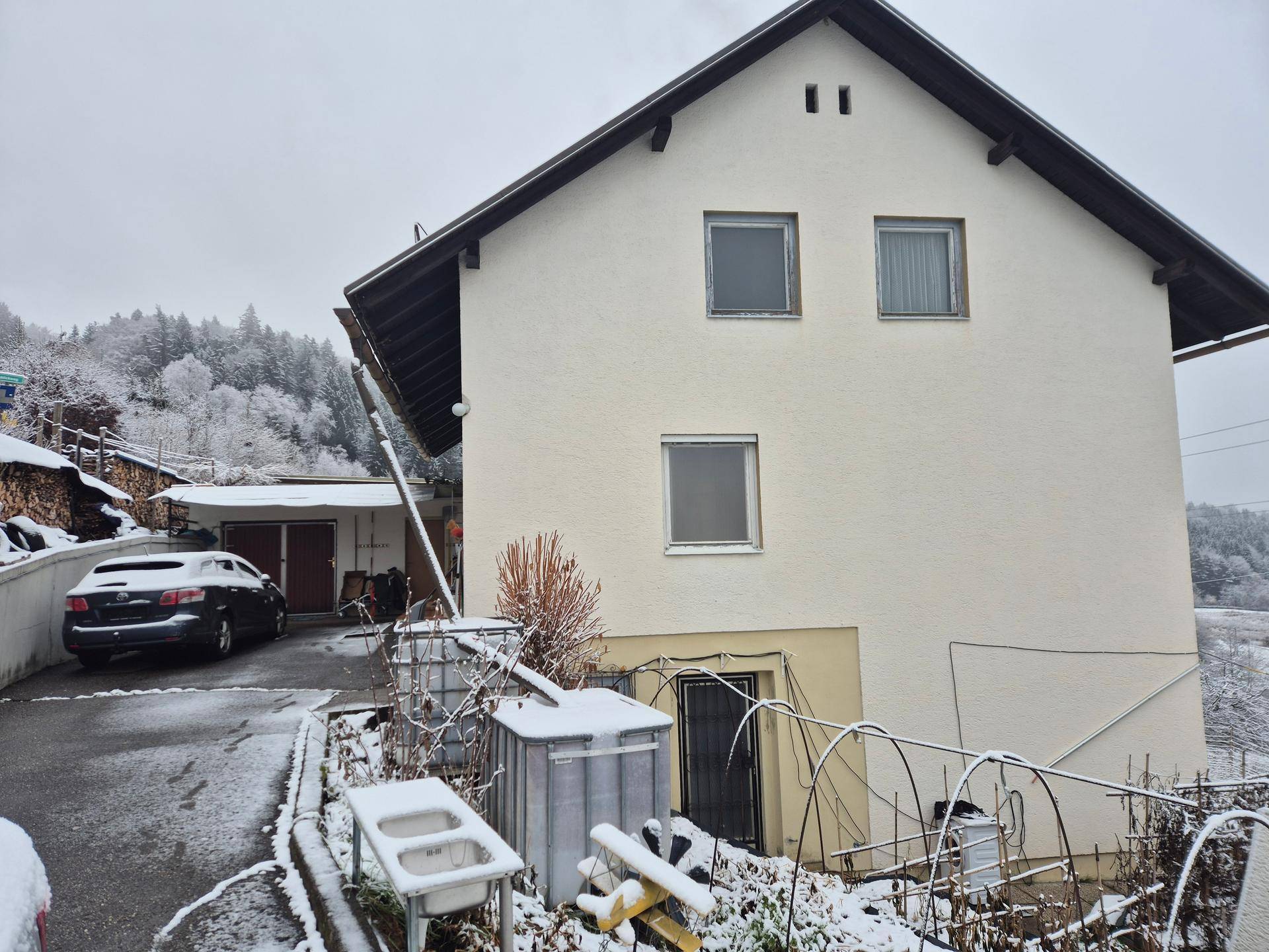 Seitenansicht des Hauses mit verschneiter Auffahrt und Garagenzugang im Winter.
