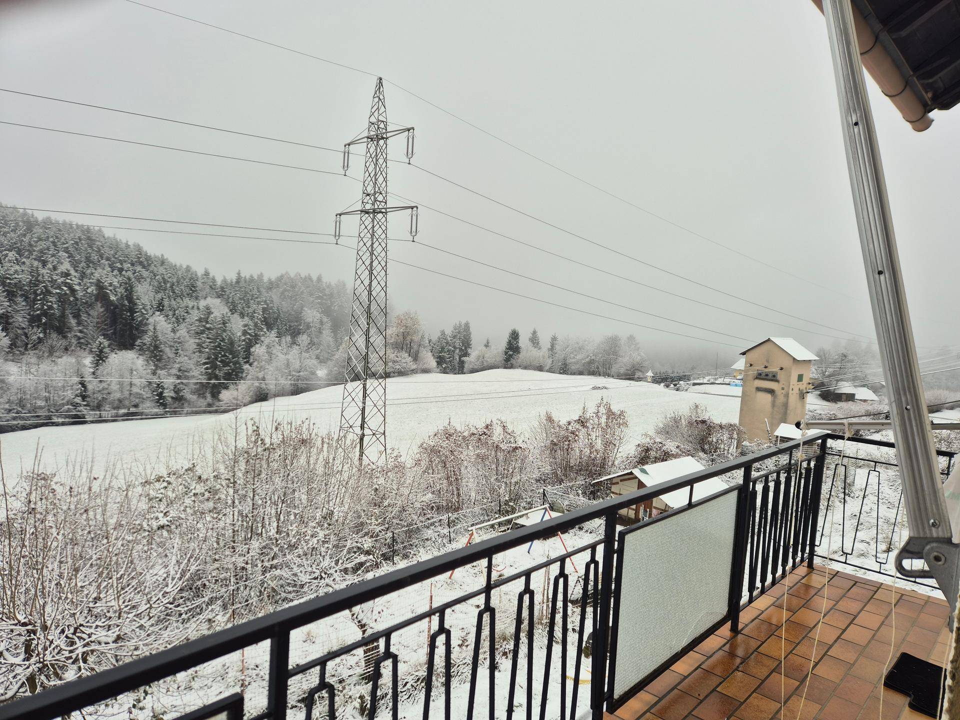 Balkon mit Terrakottafliesen und schmiedeeisernem Geländer, bedeckt mit Schnee und Blick in die Winterlandschaft.