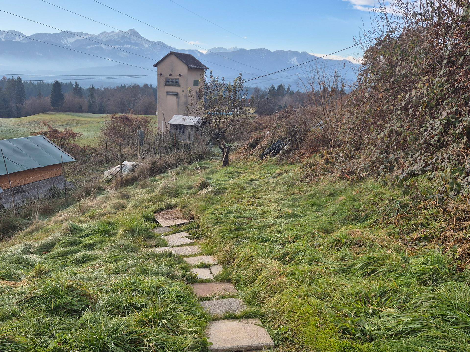 Steinpfad durch einen grasbewachsenen Hang mit Blick auf ein entferntes Gebäude und Berge.