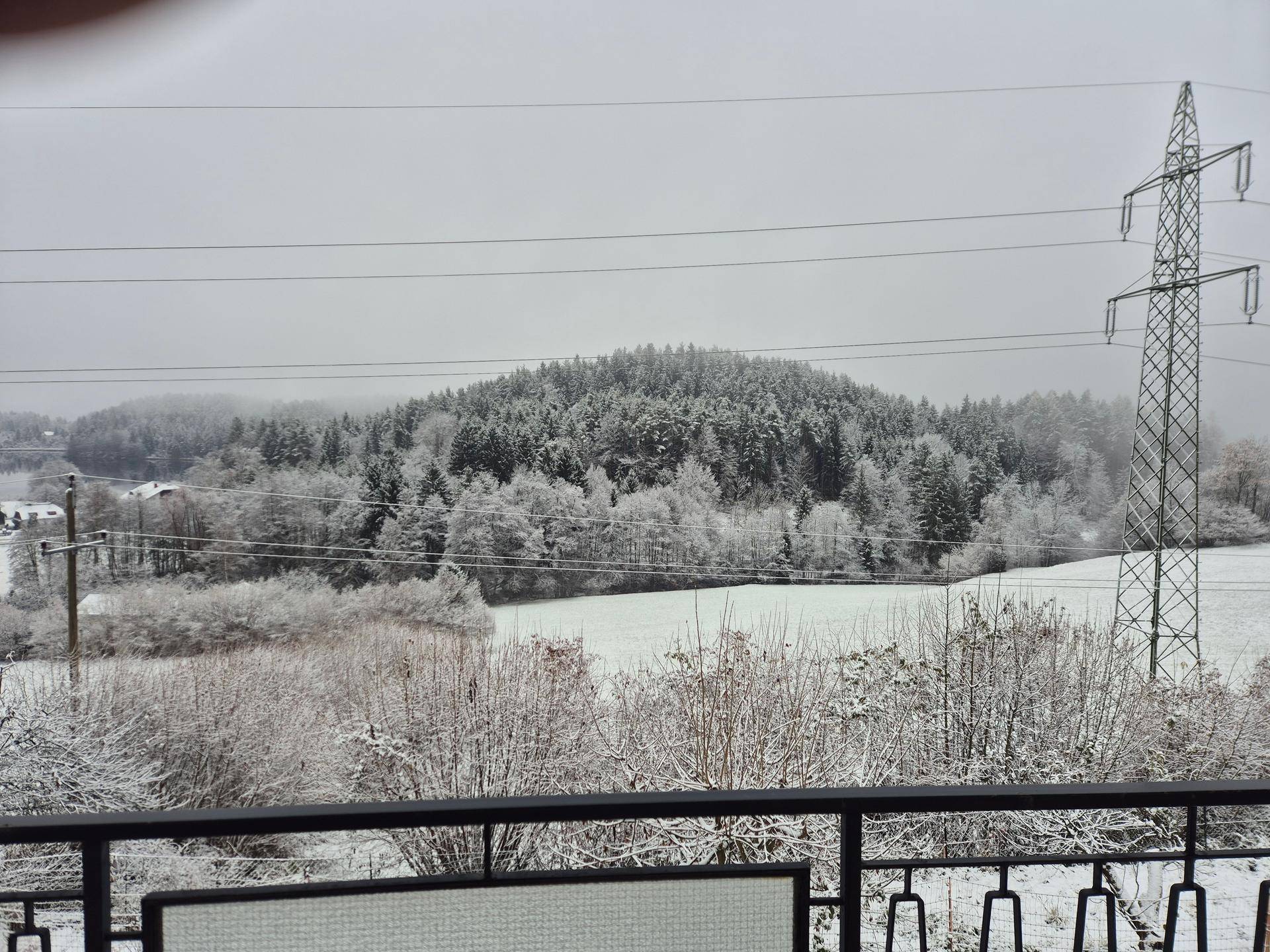 Schneebedeckte Winterlandschaft mit bewaldeten Hügeln und einem Strommast im Vordergrund.