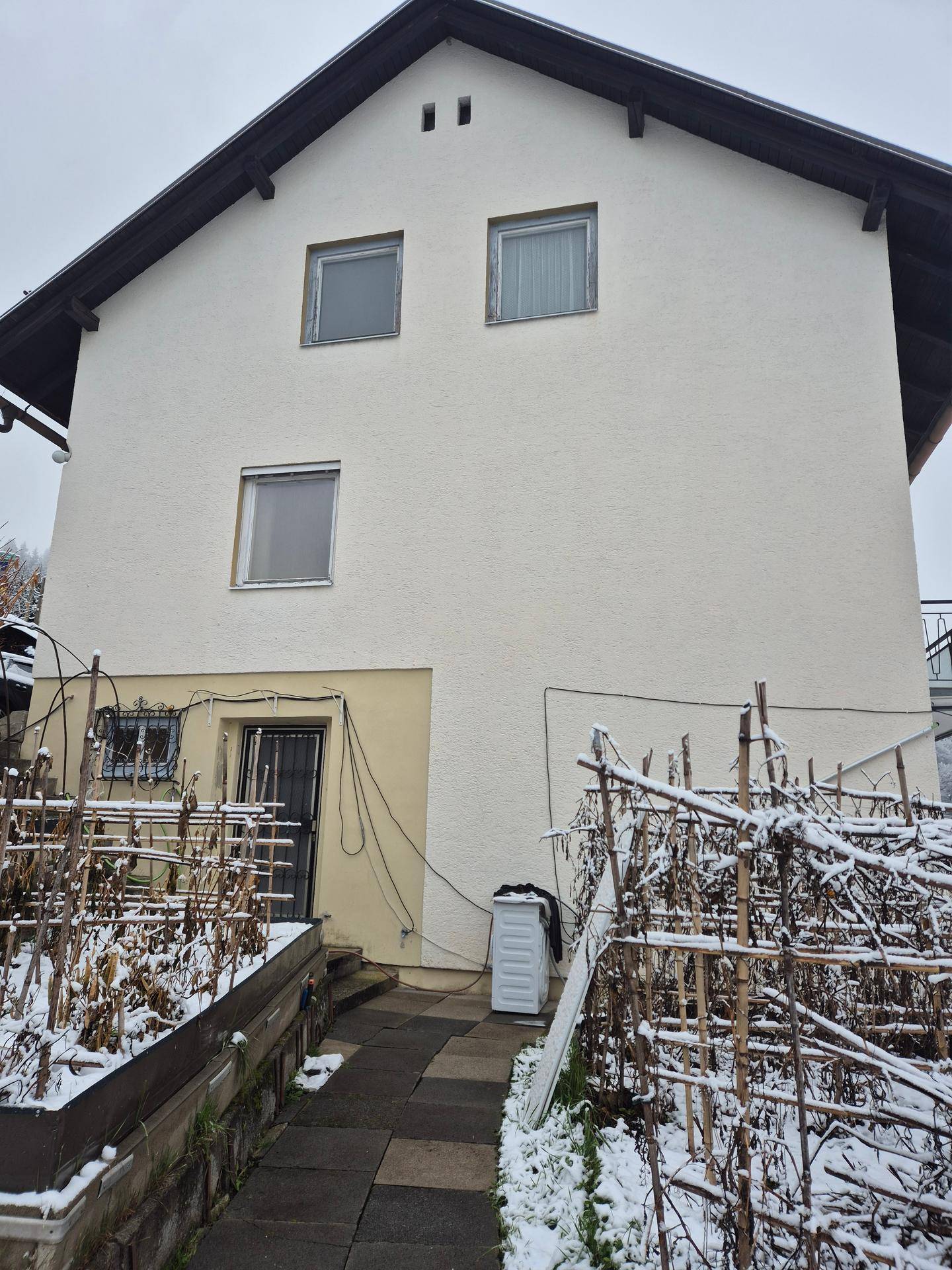 Rückansicht des Hauses mit verschneiten Gartenbeeten und einem Zugang im Winter.