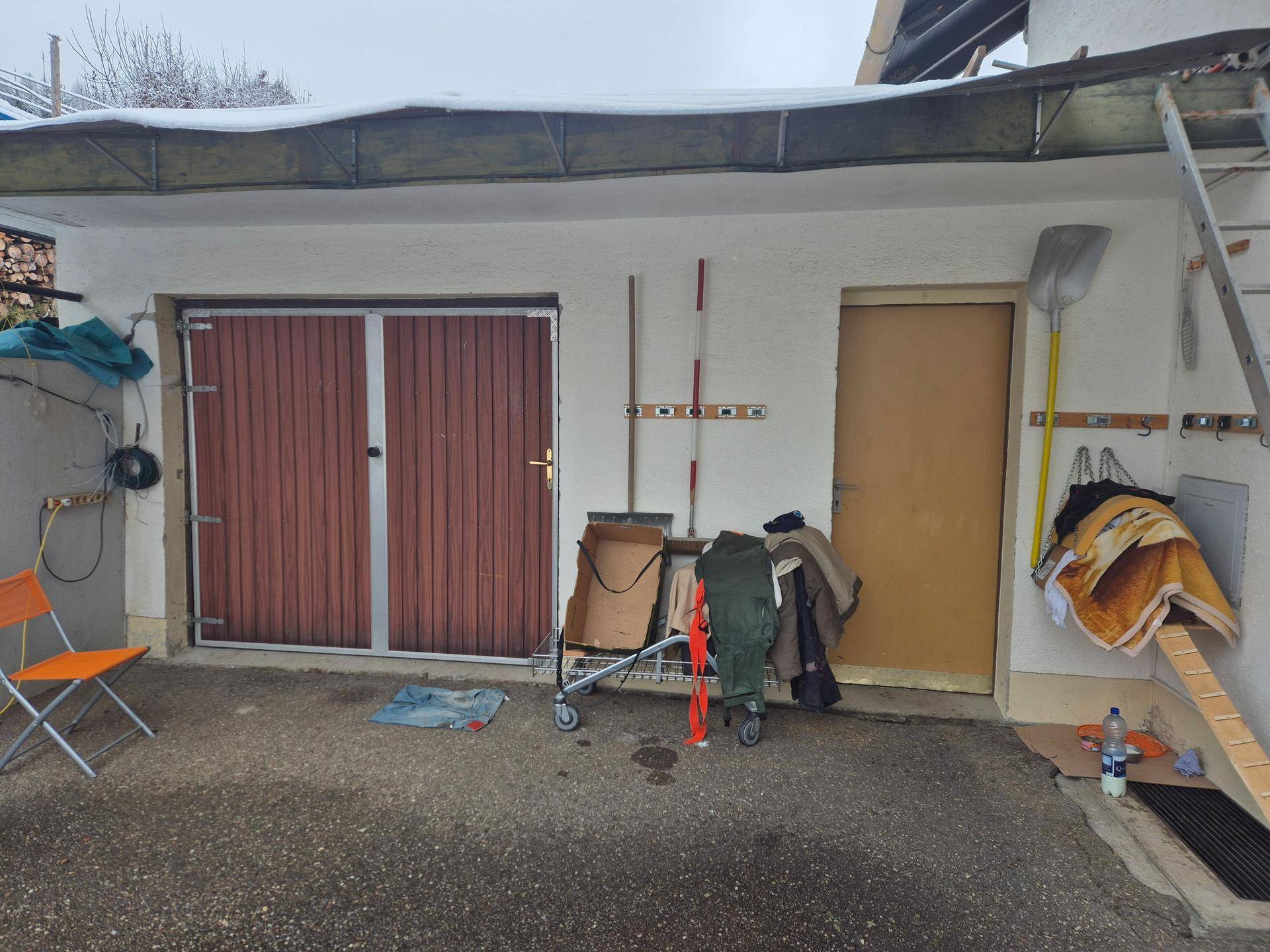Garageneingang mit braunem Tor und einer Nebentür, umgeben von Werkzeugen und Utensilien.