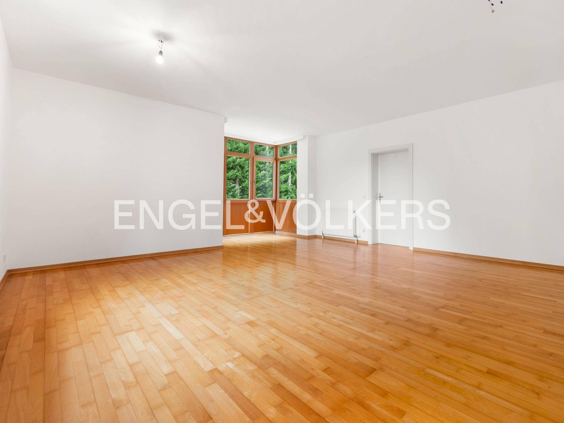 Geräumiges Wohnzimmer mit hellem Parkettboden und Zugang zu einem weiteren Bereich.
