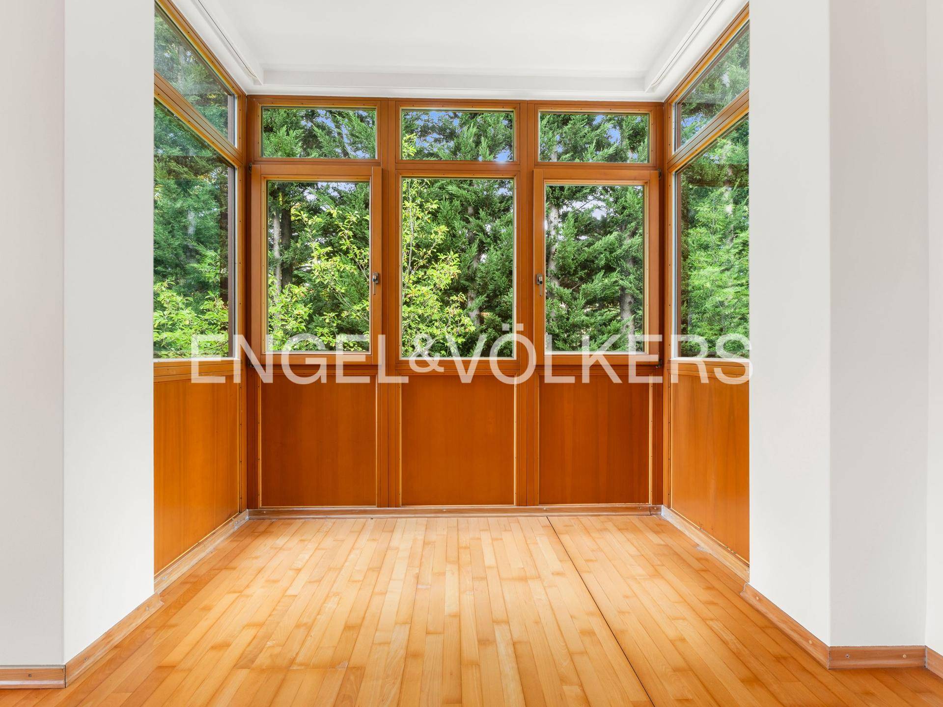 Heller Wintergarten mit Holzvertäfelung und großen Fenstern, die einen schönen Blick ins Grüne bieten.