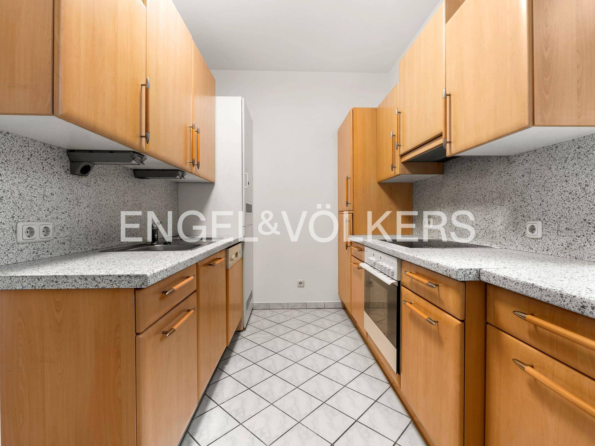 Funktionale Küche mit Holzschränken, hellen Arbeitsplatten und weiß gefliestem Boden.