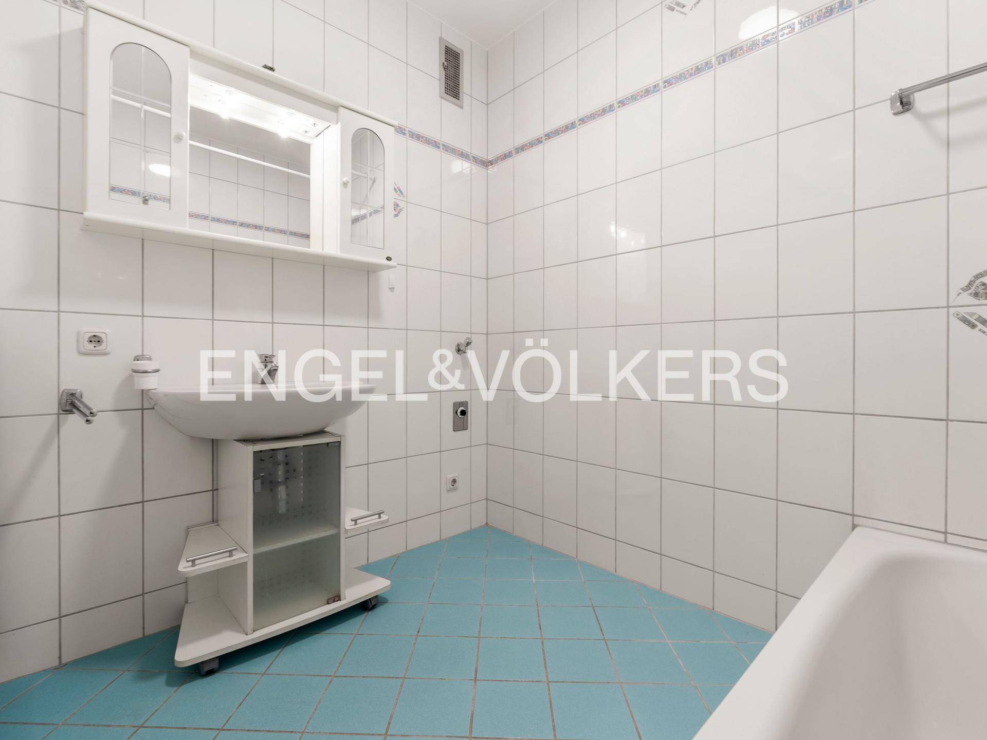 Badezimmer mit weißen Wandfliesen, hellblauen Bodenfliesen, Waschbecken und Badewanne.